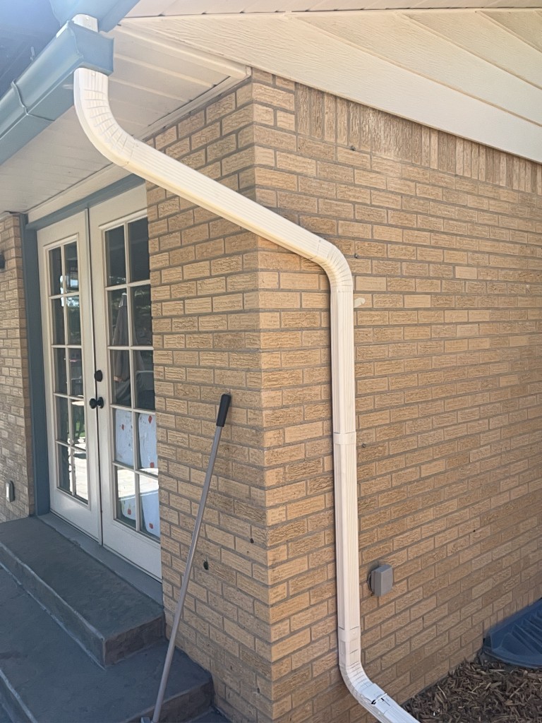 White downspout routed along a brick exterior under a teal gutter